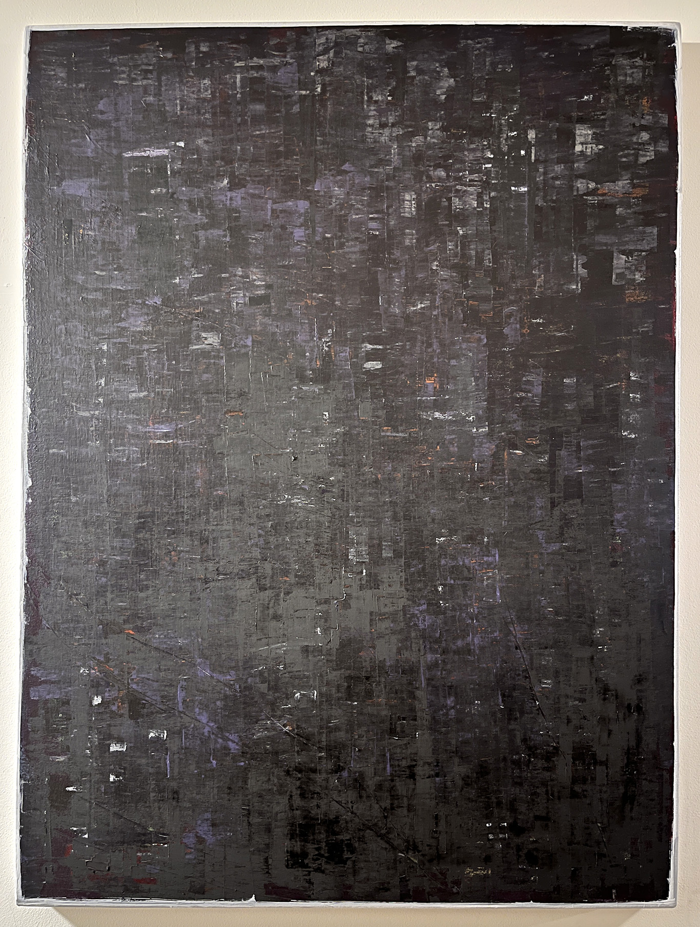 A dark abstract painting with rectangular strokes created from using a paint scraper. The main colors are black, dark grey, with flecks of dark purple and light grey.